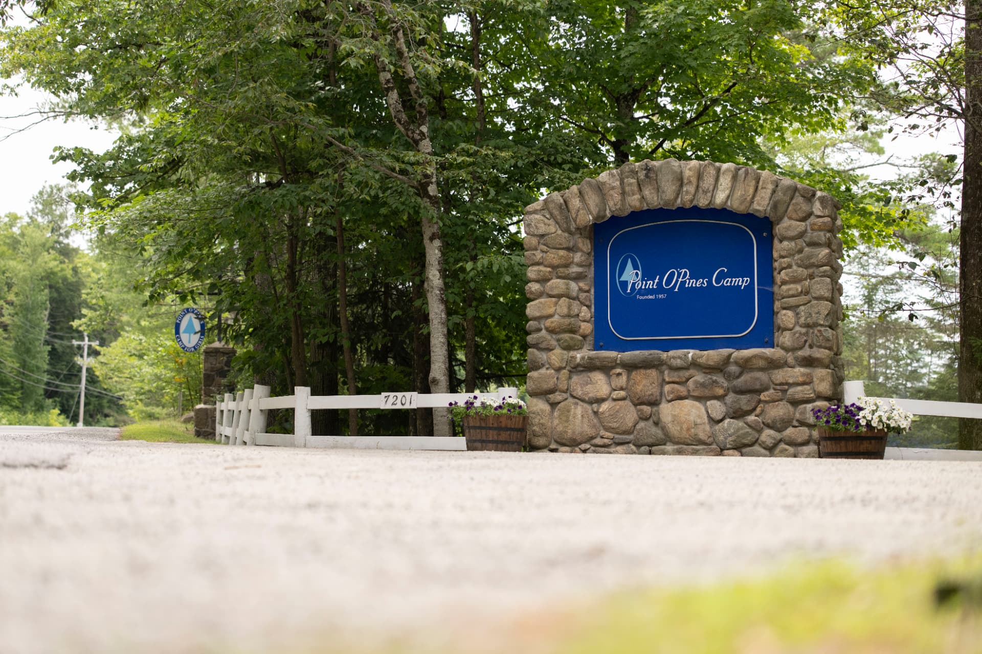 The stone entrance sign for Point O'Pines Camp on a tree-lined road