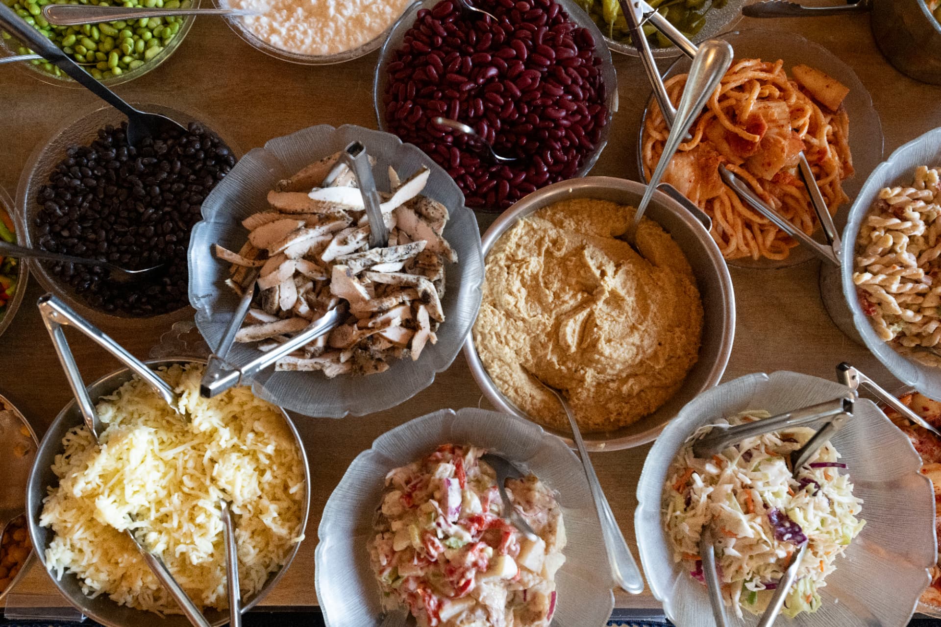A family-style buffet spread of salads, meats and sides in serving bowls on a wooden table