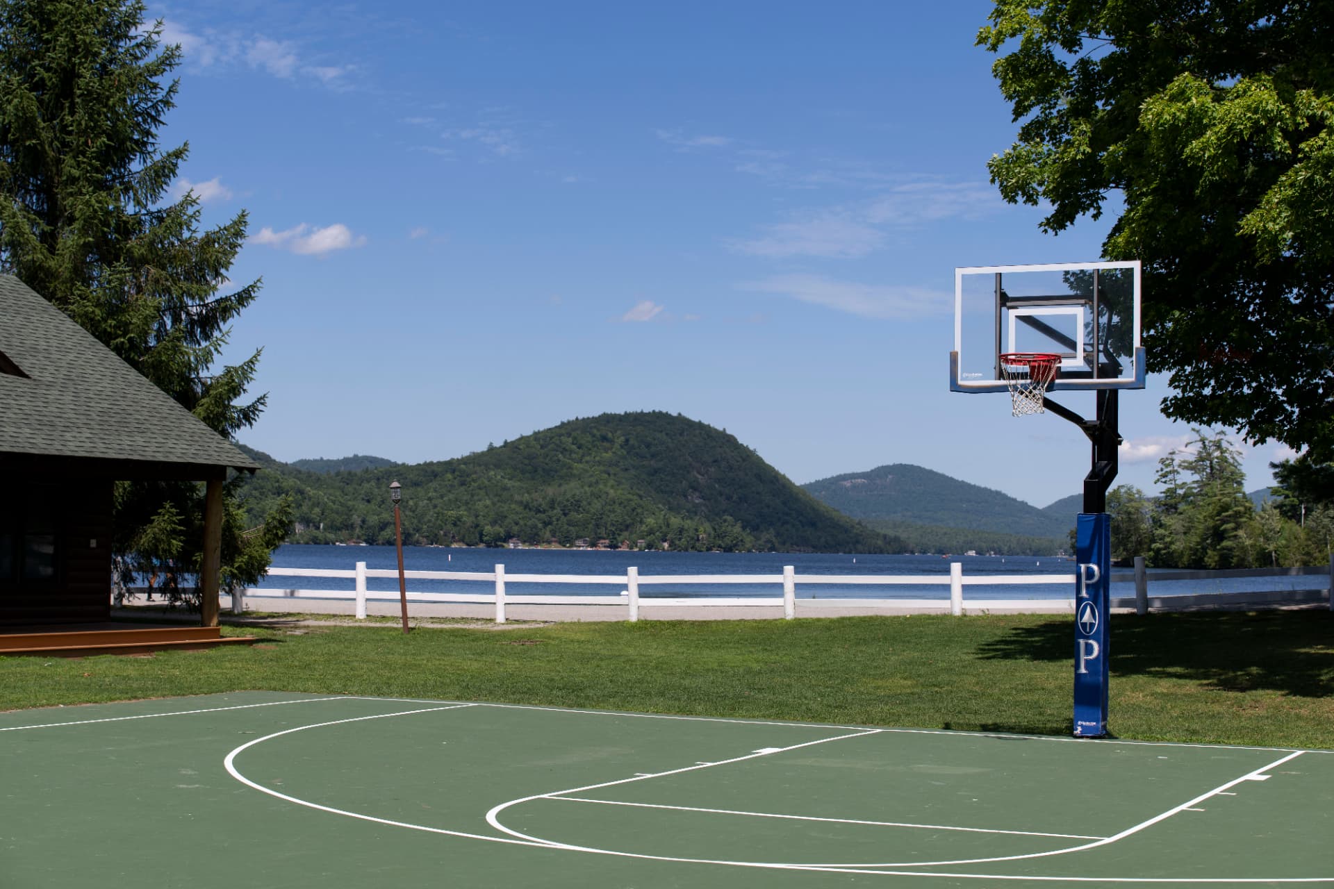 The basketball court at Point O'Pines with a white fence, lawn and Brant Lake behind
