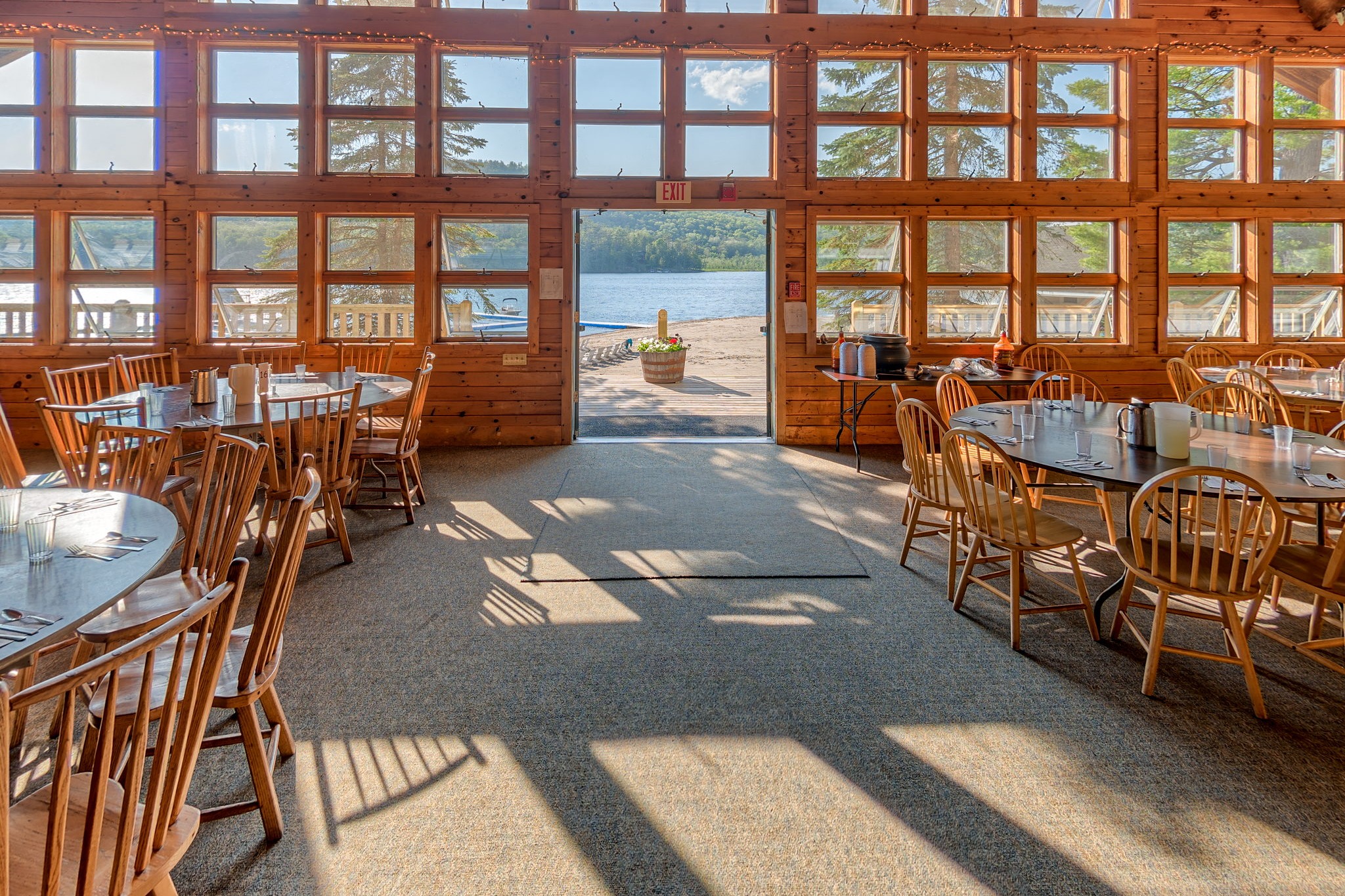 Inside the timber-roofed dining hall at Point O'Pines, with round tables and a view out to Brant Lake